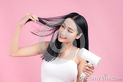 Beautiful Smiling Asian Girl With Black Long Straight Hair Using Hairdryer. Isolated on pink background Stock Photo