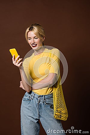 beautiful smiling blonde girl with string bag using yellow smartphone Stock Photo