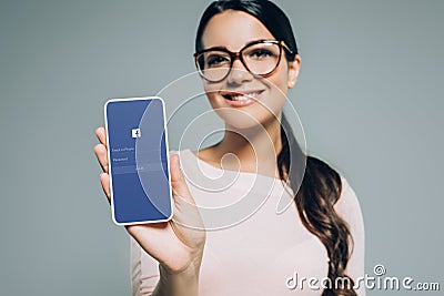 beautiful smiling girl presenting smartphone with facebook app Editorial Stock Photo