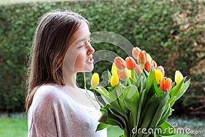 Beautiful smiling happy tween girl holding big bouquet of bright yellow and orange tulips talking to them Stock Photo