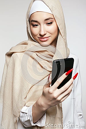 beautiful smiling islamic young woman with smartphone. Happy girl in hijab looking at the screen Stock Photo