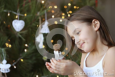 Beautiful smiling little girl decorating Christmas tree and holding angel doll in her hands Stock Photo