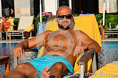 Beautiful smiling Man with sunglasses and wedding ring relaxing and lazing at pool and having a good time Stock Photo