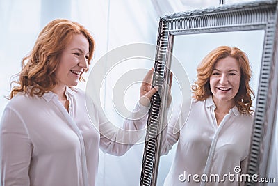 beautiful smiling mature woman standing near mirror and looking Stock Photo