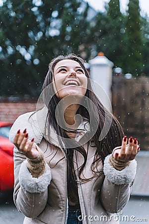 Beautiful smiling woman catches snowflakes with her hands. Female walk down street under snowfall. Warm european winter Stock Photo
