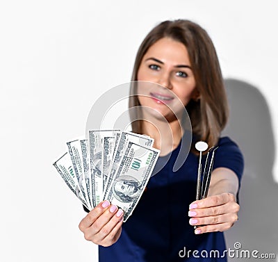 Beautiful smiling woman dentist or doctor orthodontist standing and holding dollars and dental tools in hands Stock Photo