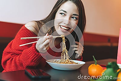 Beautiful smiling young asian woman in red clothes eating asian food with bamboo chopsticks in the chinese vietnamese restaurant Stock Photo