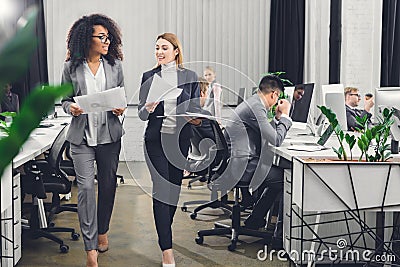 Beautiful smiling young multiracial businesswomen holding papers and walking Stock Photo