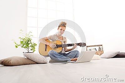 Beautiful smiling young woman playing guitar with computer, lear Stock Photo