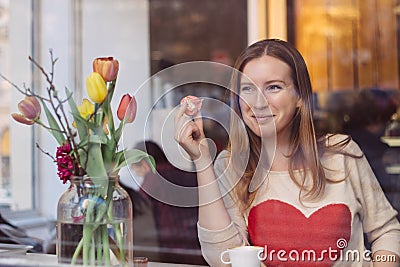 Beautiful smiling young woman sitting in coffee shop near the window,drining coffee and eating dessert Stock Photo