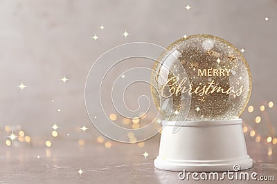 Beautiful snow globe with phrase Merry Christmas on marble table against festive lights, space for text Stock Photo