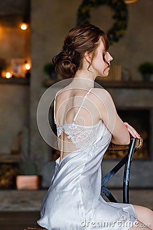 A beautiful sophisticated bride in a lace negligee sits with her back to the camera on a chair. Morning bride Stock Photo