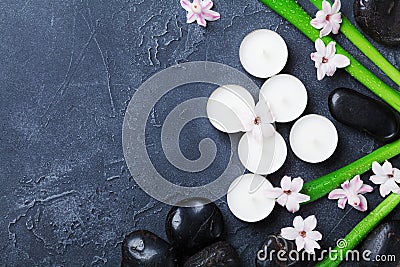 Beautiful spa background with massage pebble, green leaves, flowers and candles on black stone table from above. Aromatherapy. Stock Photo