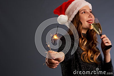 beautiful sparklers and a glass of champagne in a woman hands on gray background. Looks and smiles into the camera, isolated on Stock Photo