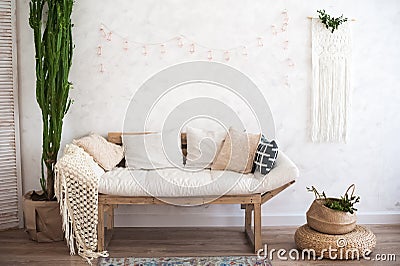 Beautiful sping decorated interior in white textured colors. Living room, beige sofa with a rug and a large cactus. Stock Photo