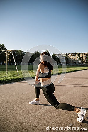 A beautiful sports girl in black sportswear is doing a warm-up at the stadium. The concept of a healthy lifestyle Stock Photo