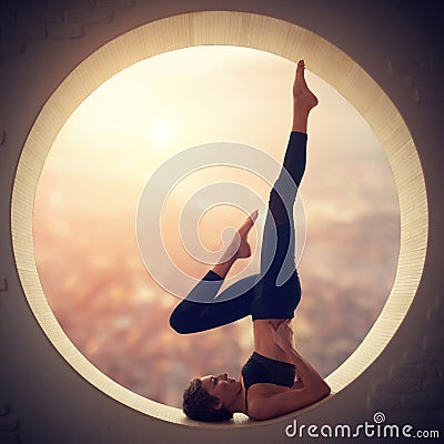 Beautiful sporty fit yogi woman practices yoga Salamba Sarvangasana - shoulderstand pose in a window Stock Photo