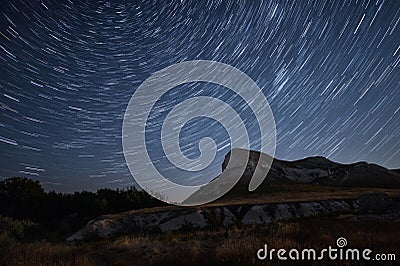 Beautiful star trails time-lapse over the hills. Polar Star at the center of rotation. Stock Photo