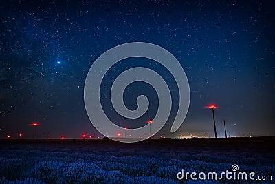 Beautiful starry night sky with milky way and blue sky over a field of lavender and red lights of wind turbines Stock Photo