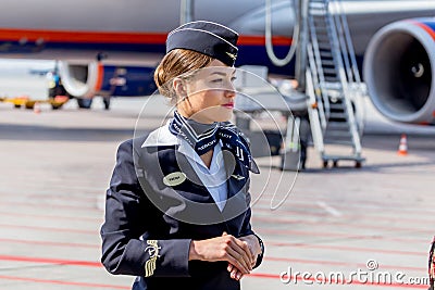 Beautiful stewardess dressed in official dark blue uniform of Aeroflot Airlines on airfield. Passenger jet aircraft on background. Editorial Stock Photo