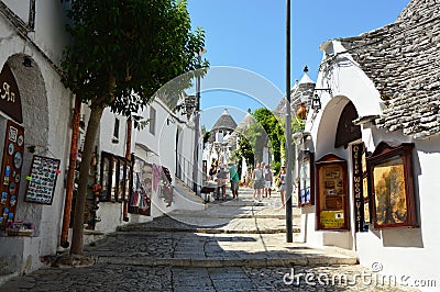 Beautiful street of Alberobello with trulli houses among green plants and flowers, main touristic district, Apulia region, Southe Editorial Stock Photo