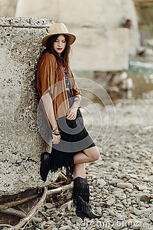 beautiful stylish boho woman with hat, leather bag, fringe poncho and boots. girl in gypsy hippie look young traveler posing near Stock Photo