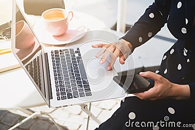 Beautiful stylish woman sitting in a street cafe drinking cappuccino and working on a laptop Editorial Stock Photo