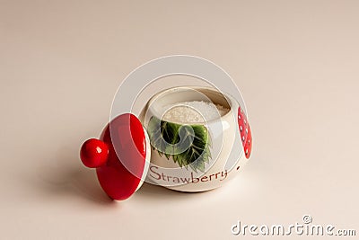 A beautiful sugar bowl with painted strawberries and a red lid, filled with white sugar on a white background Stock Photo