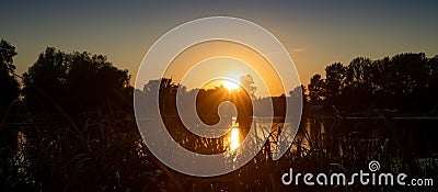 Beautiful summer autumn landscape, the sun sets in the forest, a view of the trees and grass pond, reflected in the water. Stock Photo