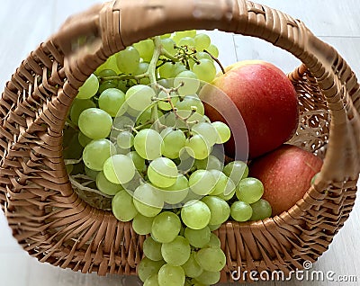 Beautiful summer fruits in a basket. Yellow red apples and white grapes. Stock Photo