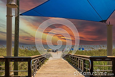 A beautiful summer landscape at the beach with a wooden footpath, people relaxing on the beach with colorful umbrellas, blue ocean Editorial Stock Photo