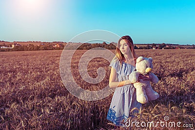 Beautiful summer woman wheat field, blue dress, hands of children`s toy teddy bear. Free space for text. Rest rural Stock Photo
