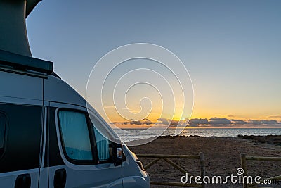 Beautiful sunrise with a gray camper van with a pop up roof parked at the beach Editorial Stock Photo