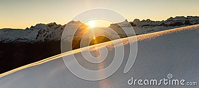 Beautiful sunrise in snowy mountain landscape. Sunbeams illuminating unspoiled powder snow. Alps, Switzerland. Stock Photo