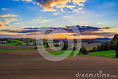 Beautiful sunset over countryside landscape of rolling hills with sun beams piercing sky and lighting hillside Stock Photo