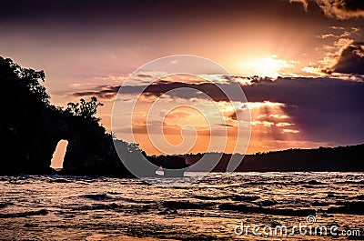 Beautiful sunset over the ocean with small island. Sun passing behind clouds with sunrays. Bali Stock Photo
