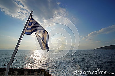 Beautiful sunset over the sea with the Greek flag in the foreground viewed from the ferry on the route to Mykonos in the Cyclades Stock Photo