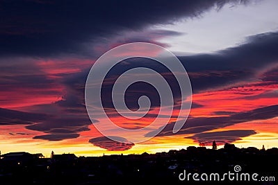 Beautiful sunset with red ribbon clouds like roses. Red-blue sunset over the city with dark clouds. Dark silhouette of the city Stock Photo