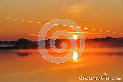 Beautiful sunset is reflecting on the lake. Sky with orange and yellow clouds. Majestic spring morning. Foggy forest Stock Photo