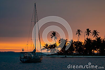 Beautiful sunset with silhouette of sailboat and palm trees on island. Vacation and adventure concept Editorial Stock Photo