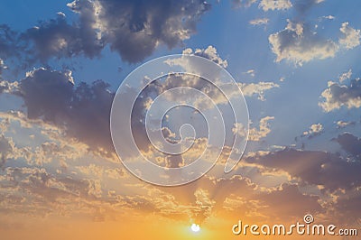 Beautiful sunset or sunrise with sun and orange, grey clouds on the blue sky Stock Photo