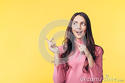 Beautiful surprised woman pointing finger at copy space looking away isolated on yellow background Stock Photo