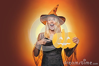 Beautiful surprised woman in witches hat and costume - showing products. Halloween Woman portrait. Beauty Woman posing Stock Photo