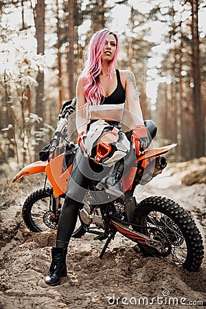 Modern tattooed hipster girl with bright pink hair sitting on her motocross bike in woods Stock Photo