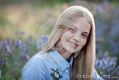 Beautiful teen girl with braces on her teeth smiling. portrait of blonde model with long hair in blue flowers Stock Photo