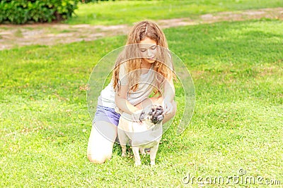 Beautiful teen girl feeding a pug dog outdoors in a park Stock Photo