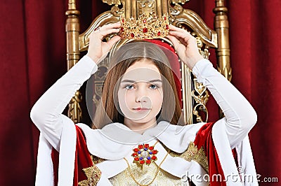 Beautiful teen girl holding crown sitting in vintage armchair Stock Photo