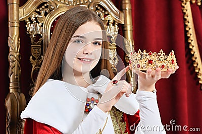 Beautiful teen girl holding crown sitting in vintage armchair Stock Photo