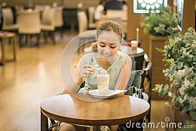 Beautiful teen girl stirring cream in coffee in tall glass at cafe Stock Photo