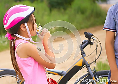 Beautiful teenage boy in protective bicycle helmet and girl in a park, boy giving flowers to the girl. Friendship Stock Photo